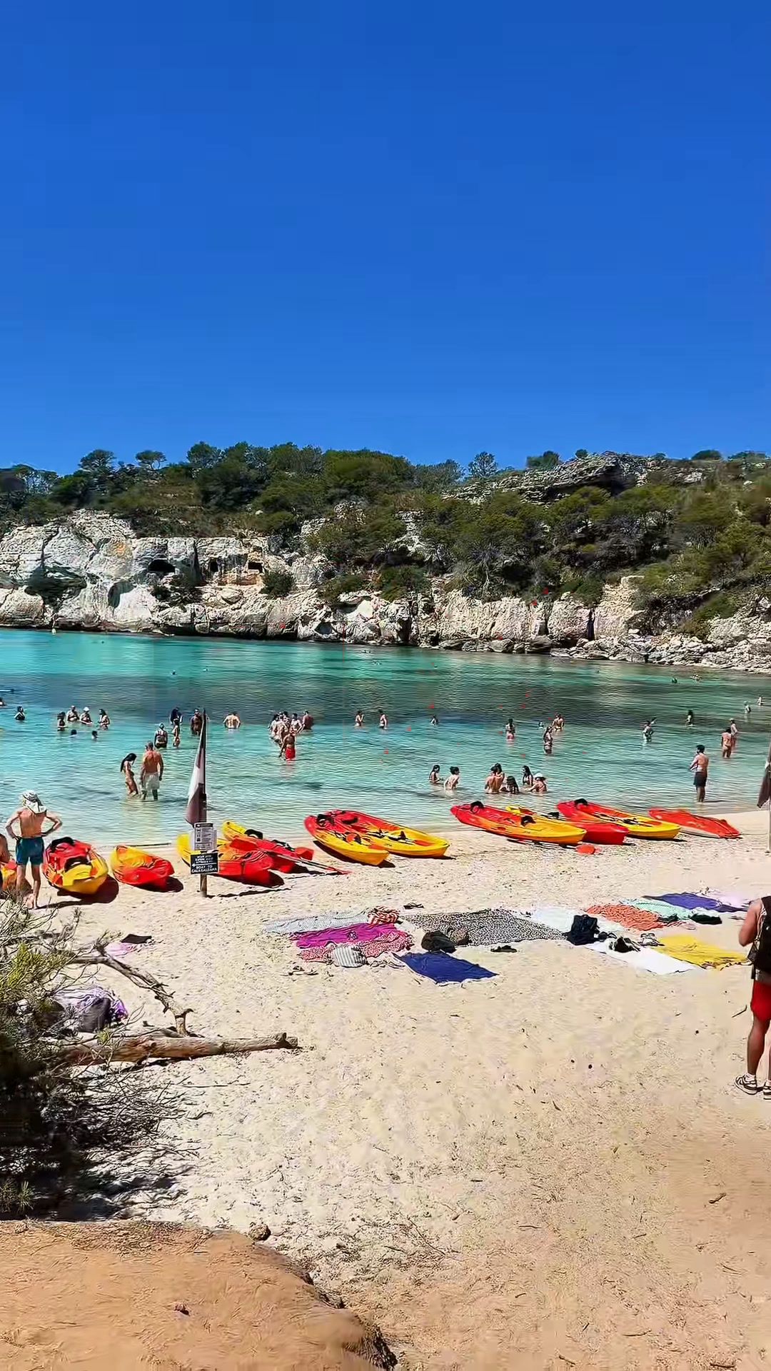 Cala Macarella desde la arena, con agua turquesa, pinos en los acantilados y kayaks en la orilla