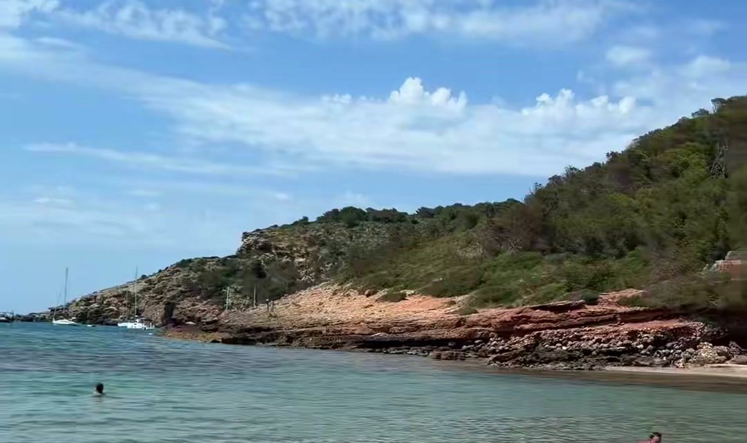 Rocas rojizas y pinar sobre el agua transparente de Es Tancats